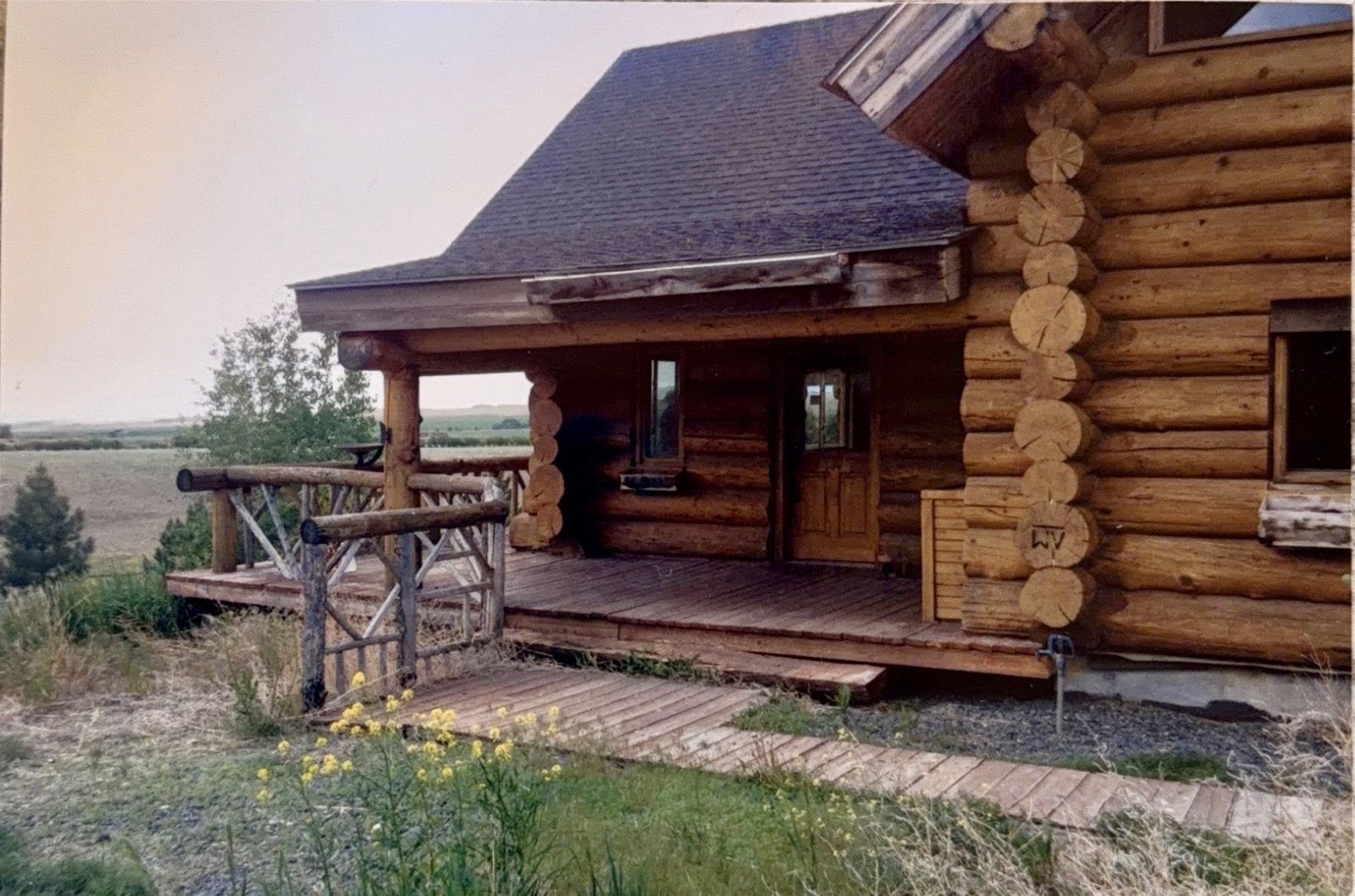 The log cabin porch, prairie rolling out behind it.