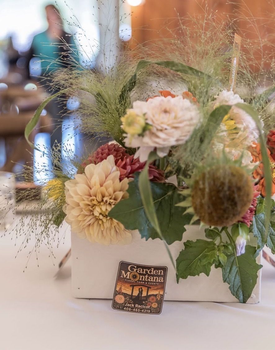 A farm-grown centerpiece of dahlias and wild grasses on a reception table, with a GardenMontana card