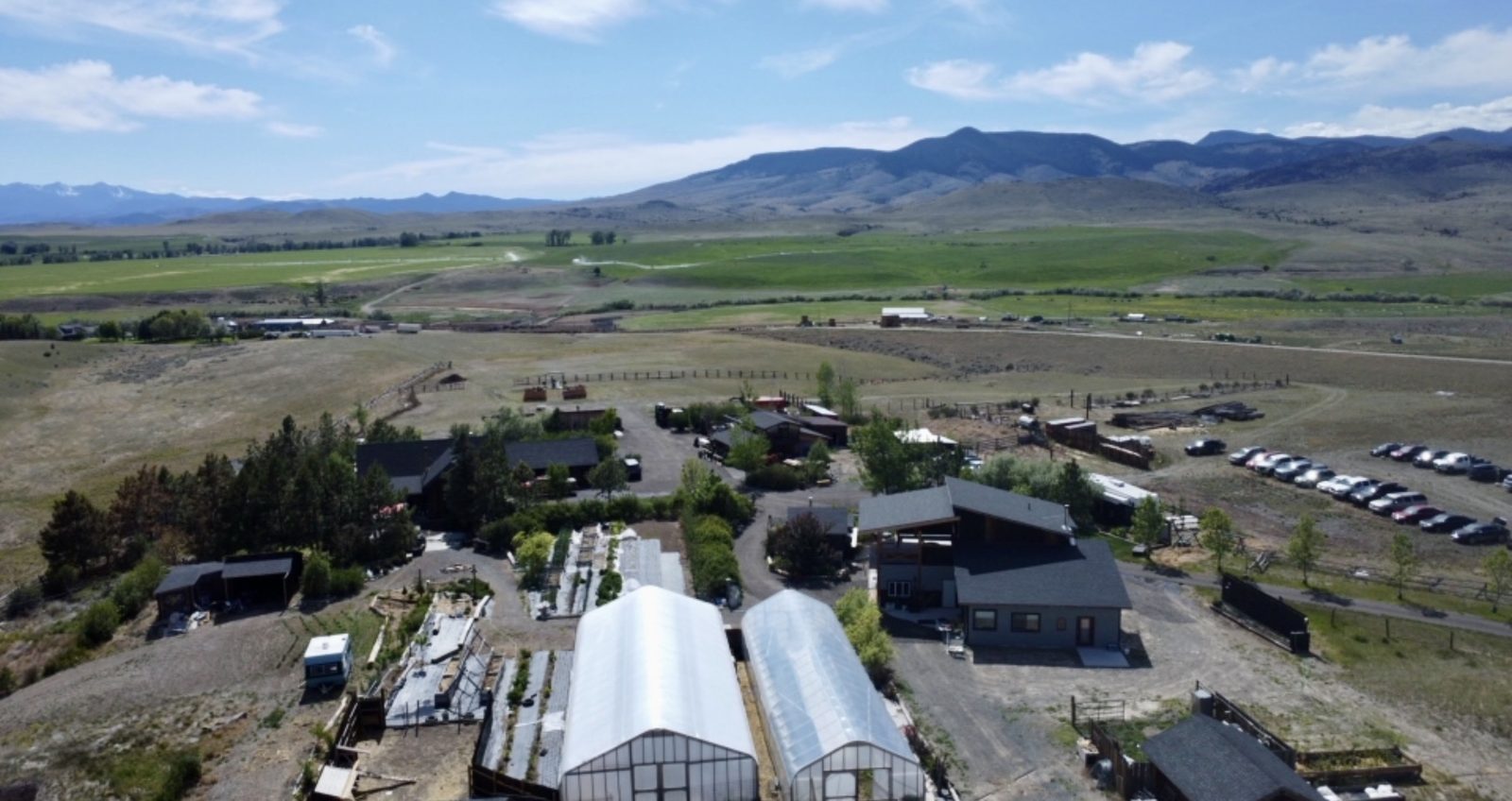 Aerial view of the farm: greenhouses, flower beds, the Bourbon Barn and stays, with the Jefferson River Valley and mountains beyond