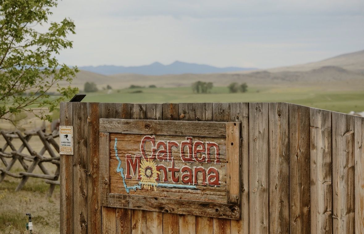 The hand-painted GardenMontana sign on the weathered board fence, the valley and mountains beyond