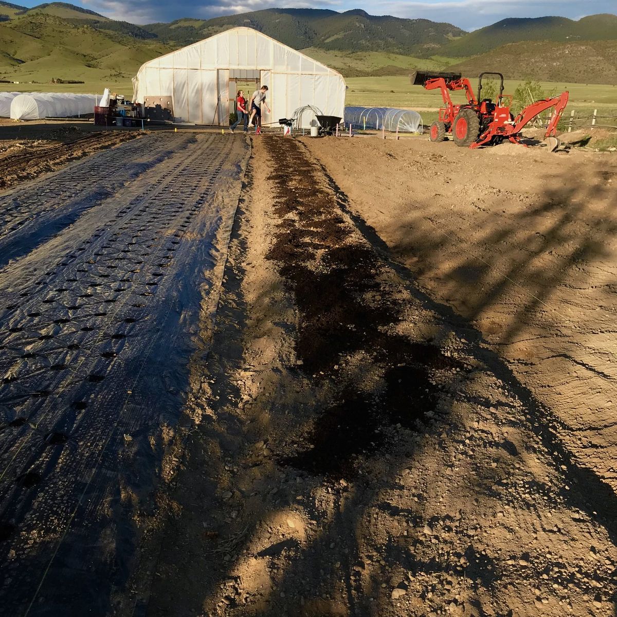 Preparing new flower beds beside the greenhouse, with the tractor parked nearby and green hills behind