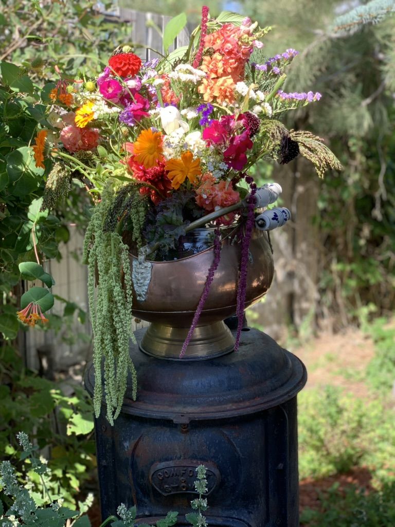 A copper pot overflowing with dahlias, zinnias and trailing amaranth, set on an old cast-iron stove in the garden