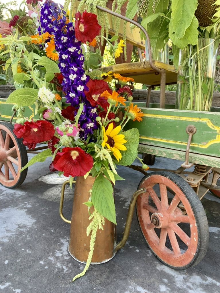 A copper pitcher of delphinium, hollyhocks, black-eyed Susans and hanging amaranth on the old green farm wagon