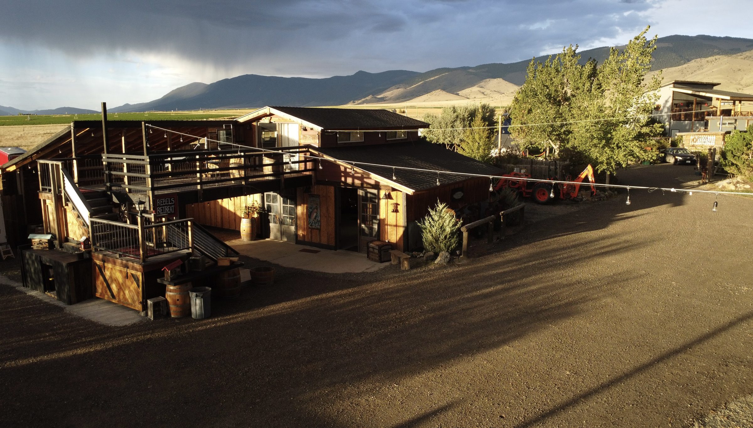 The Bourbon Barn and its deck in golden evening light, string lights overhead and storm clouds over the mountains