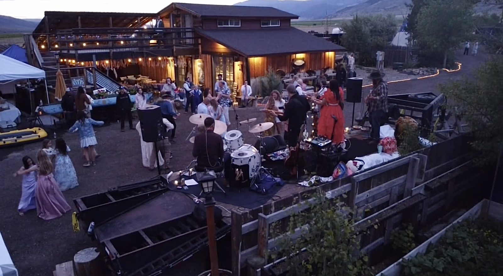 A live band playing at dusk outside the Bourbon Barn as wedding guests and kids dance under string lights