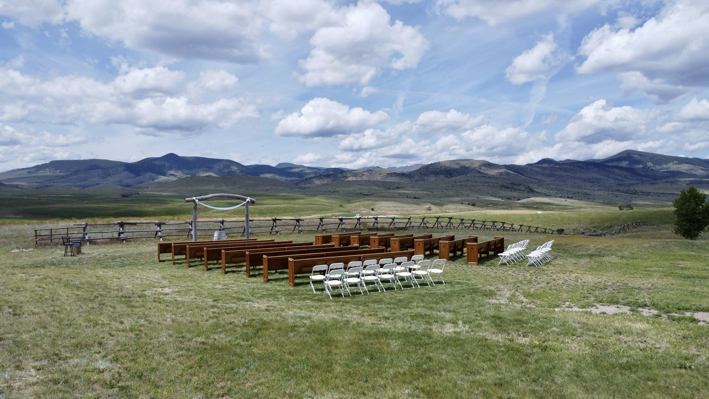 Aerial view of outdoor wedding ceremony setup with wooden pews and mountain backdrop